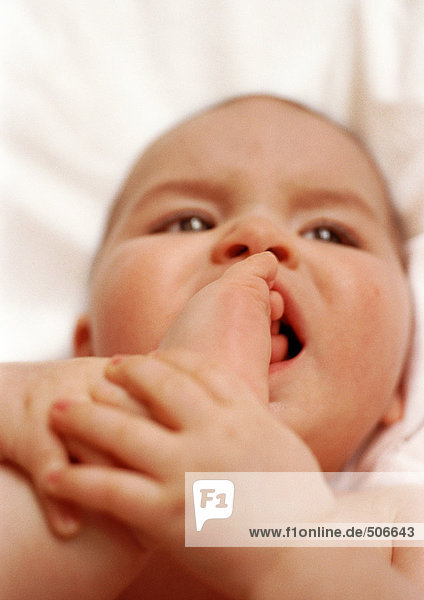 Baby lying on back  putting foot in mouth  close-up.