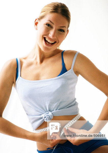 Woman smiling  measuring waist with measuring tape.