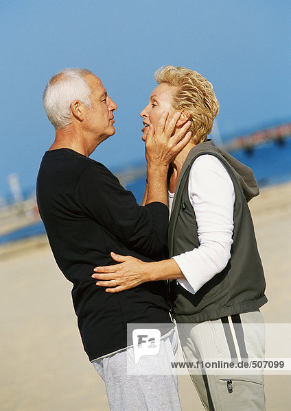 Mature couple standing on beach  embracing  side view