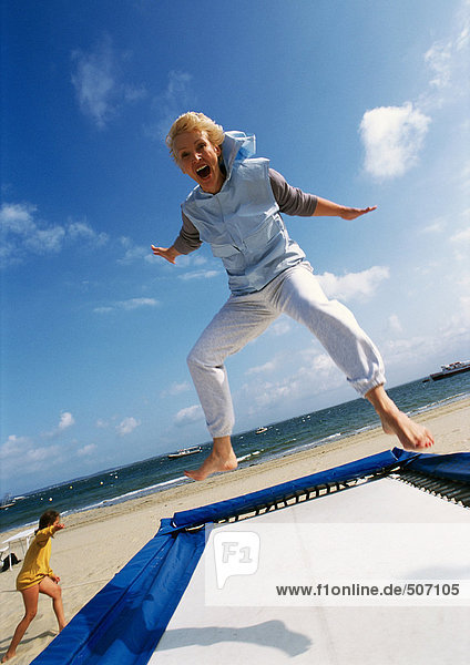 Mature woman jumping on trampoline at the beach