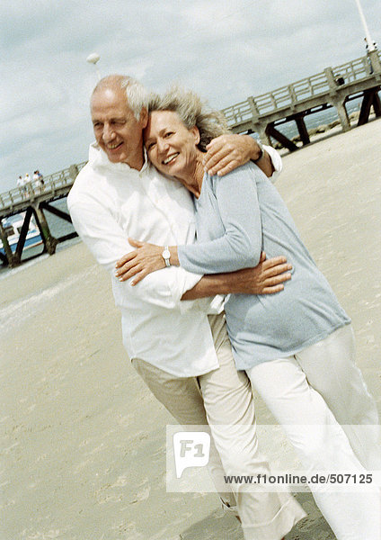 Ein reifes Paar  das am Strand mit den Armen umherläuft.