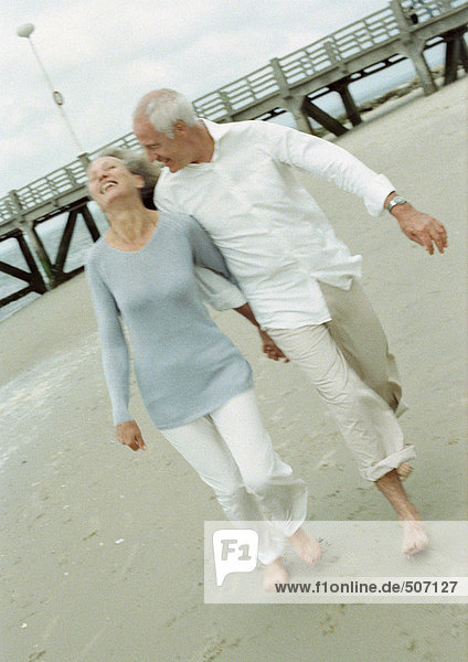 Ein reifes Paar  das barfuß geht und am Strand Händchen hält.