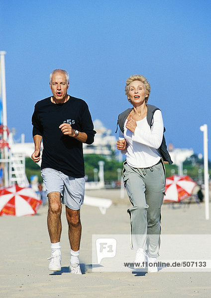 Mature couple jogging on beach  front view  full length