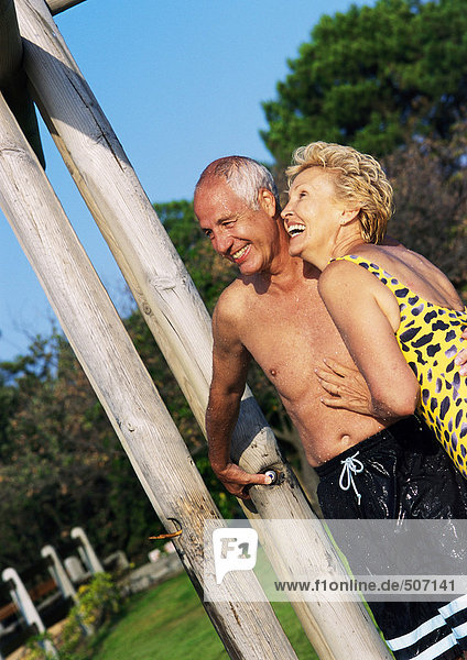 Mature man and woman standing in bathing suits in outdoor shower.