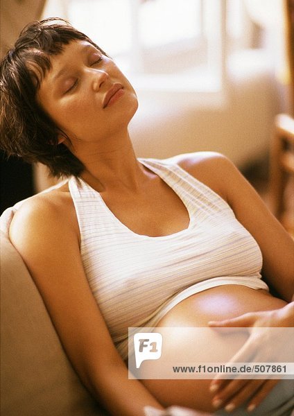 Pregnant woman sitting in armchair  eyes closed and hand on belly