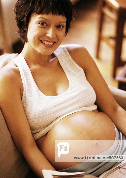 Pregnant woman sitting in armchair  smiling at camera  portrait