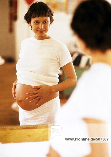 Schwangere Frau  die sich selbst im Spiegel betrachtet