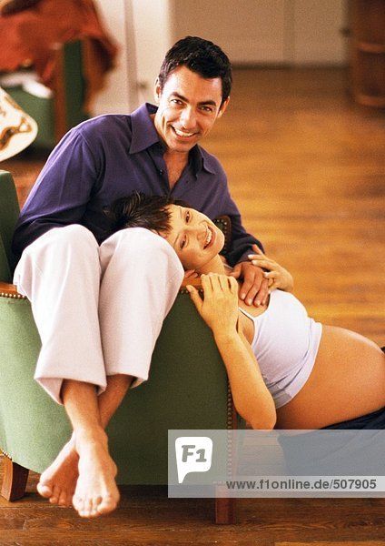 Mann rückwärts auf Stuhl sitzend und schwangere Frau auf dem Boden sitzend  Kopf auf Mann lehnend  Portrait