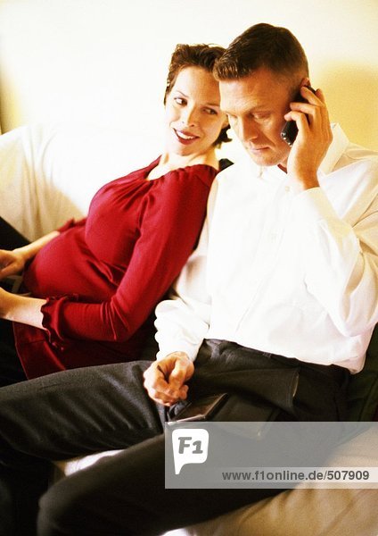 Schwangere Frau  die sich gegen einen Mann lehnt  der am Handy spricht