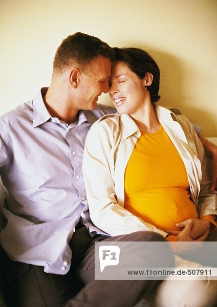 Mann und schwangere Frau sitzen und lächeln sich an.