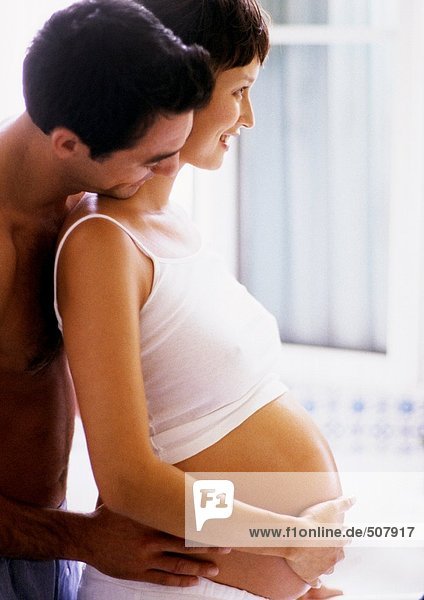Man holding pregnant woman's waist and looking over her shoulder  side view