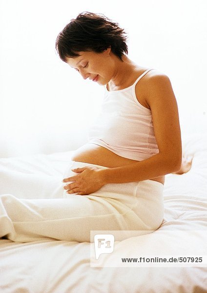Pregnant woman sitting on bed  looking at her stomach