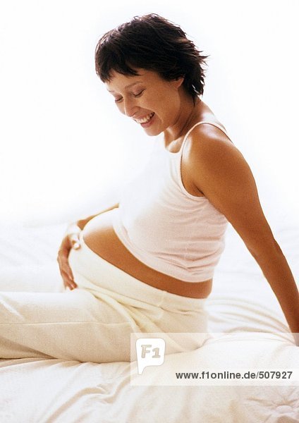 Pregnant woman sitting with hand on stomach  smiling