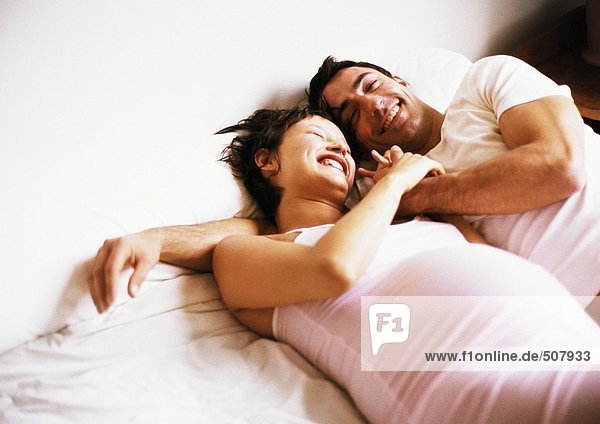Man and pregnant woman side by side on bed