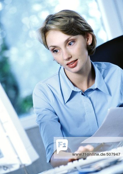 Geschäftsfrau hält Dokument  schaut auf Computer