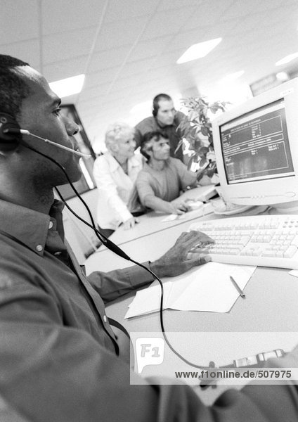 Man with headset using computer  colleagues in blurred background  B&W