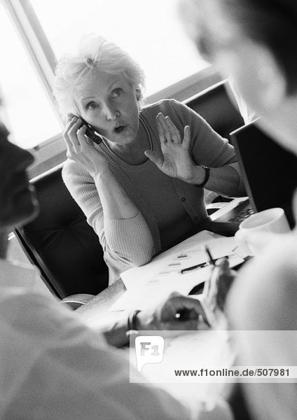 Mature businesswoman using cell phone  colleagues in blurred foreground  B&W