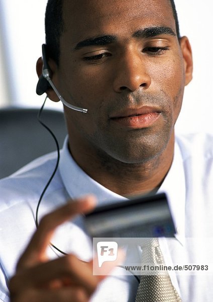 Businessman wearing headset  looking down at credit card in hand  close-up