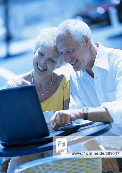 Mature woman and man sitting at a cafe terrasse with laptop computer