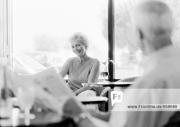 Mature man and woman looking at each other across the room in a cafe  blurred foreground  B&W
