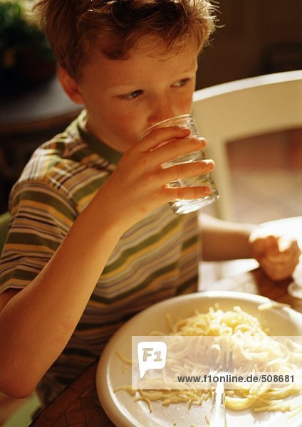Kind am Tisch sitzend mit Spaghettiteller  trinkend