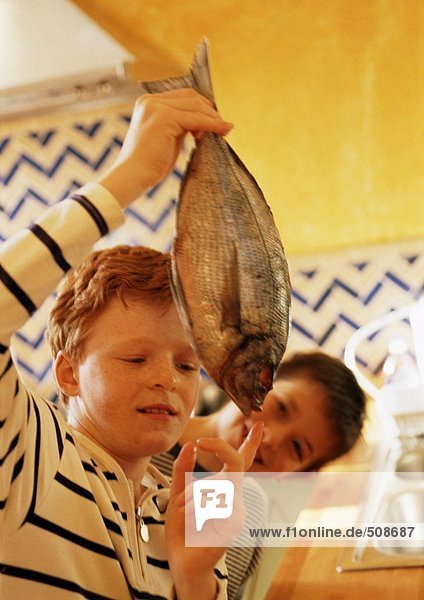 Zwei Kinder in der Küche  eines hält einen Fisch hoch.