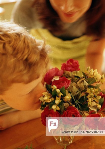 Junge riecht Blumen in Vase  Frau im Hintergrund
