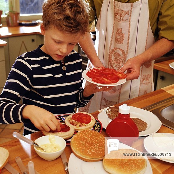 Child garnishing hamburgers  adult holding plate of tomato slices