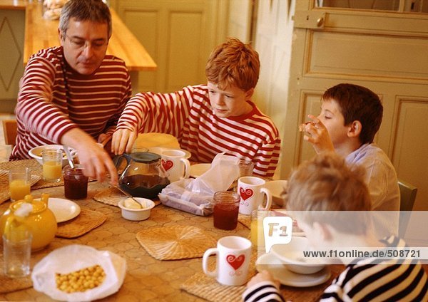 Mann und Kinder sitzen am Tisch und frühstücken.