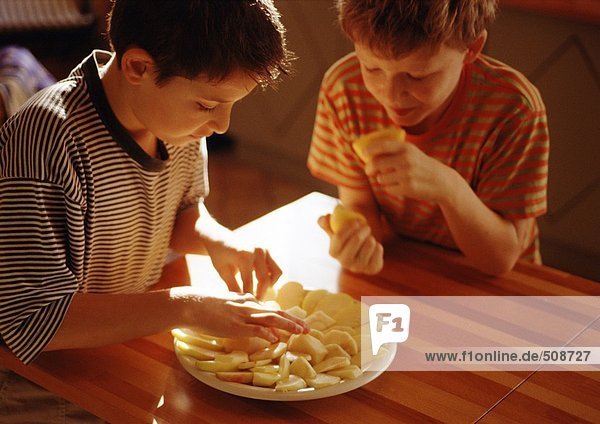 Ein Kind legt Apfelscheiben auf den Teller  das zweite Kind hält Zitronenhälften.
