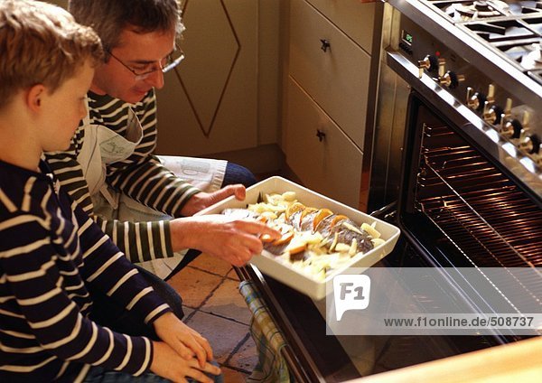 Mann und Kind stellen Kasserolle in den Ofen