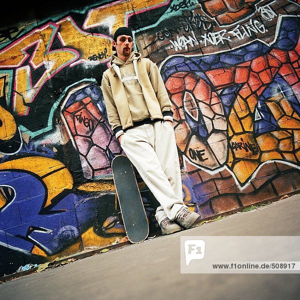 Junger Mann mit Skateboard an der Wand gelehnt  Portrait