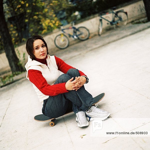 Junge Frau auf Skateboard sitzend  Portrait
