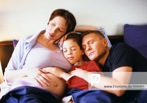 Schwangere Frau sitzend mit Mann und Kind im Bett
