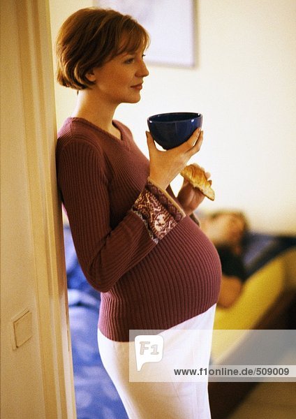 Schwangere Frau stehend mit Schale und Croissant  Seitenansicht