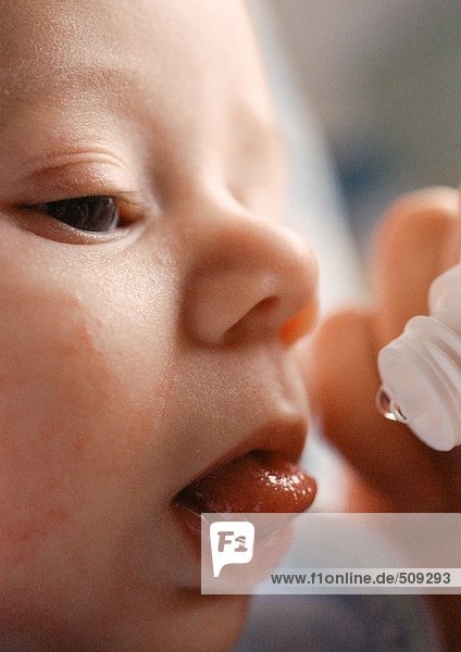 Baby's face and end of vitamin dropper  close-up