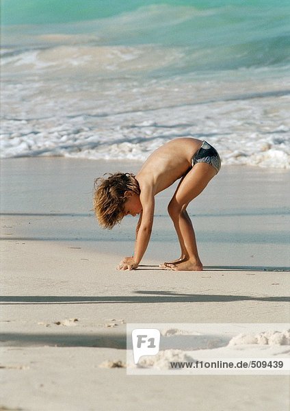 Kleines Mädchen bückt sich am Strand  Hände im Sand