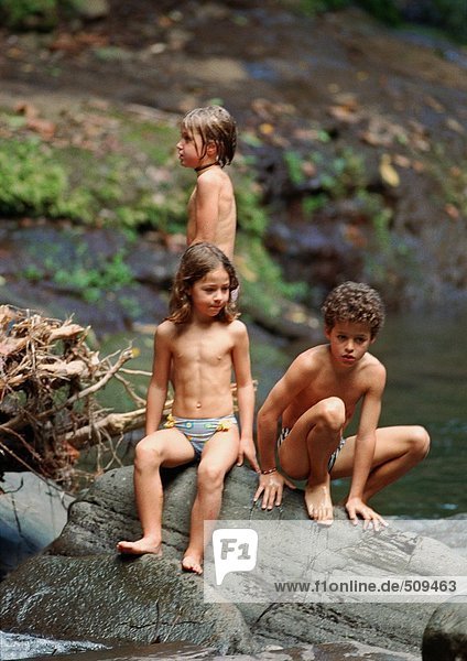 Junge und zwei Mädchen in Badehose auf einem großen Felsen  draussen