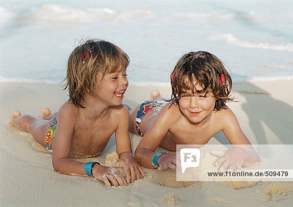 Zwei Mädchen auf Sand am Strand liegend  lächelnd