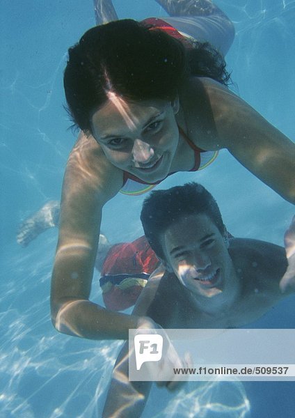 Nahaufnahme einer jungen Frau  die über einem jungen Mann im Pool  unter Wasser schwimmt.