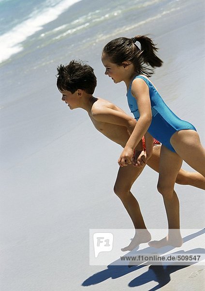 Kleiner Junge und Mädchen  die am Strand rennen.