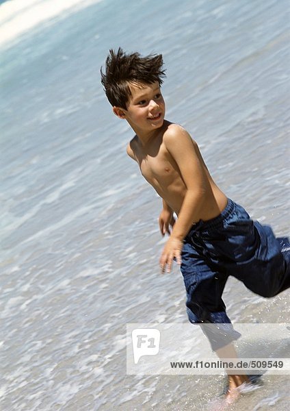 Young boy running in water at the beach.