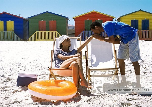 Frau am Strand sitzend,  Mann küsst ihre Hand