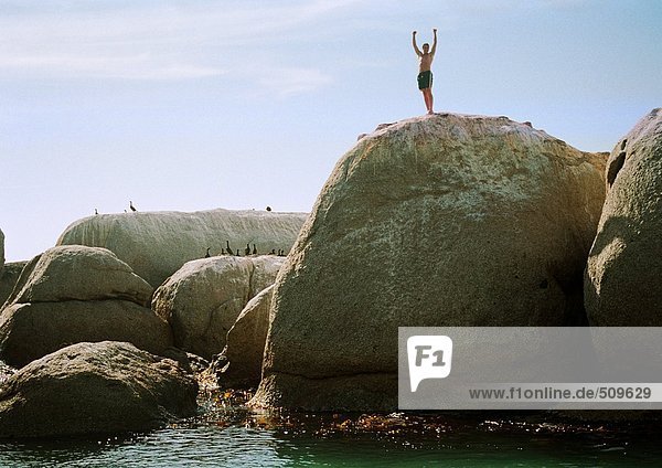 Mann steht auf einem Felsen mit Blick auf das Meer
