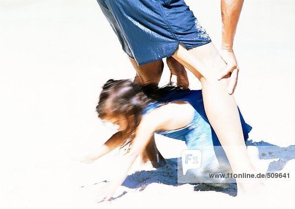 Mädchen krabbelt durch Männerbeine am Strand  verschwommen