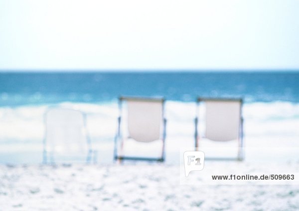 Drei Liegestühle am Strand aufgereiht  Meer im Hintergrund  verwischt