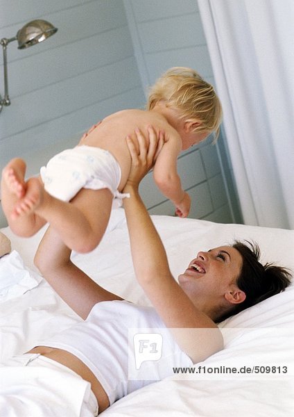 Frau auf dem Bett liegend  Baby in der Luft haltend