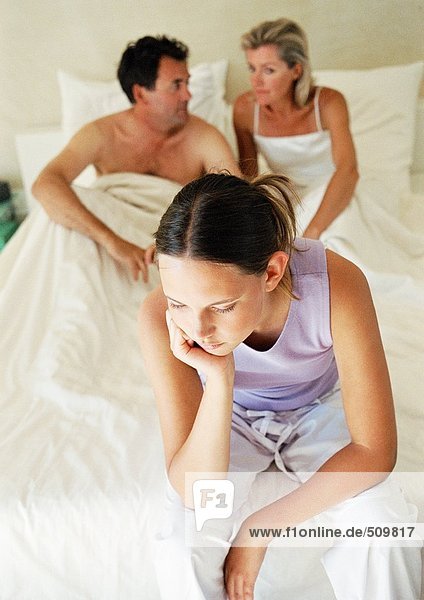 Teenagermädchen auf dem Bett der Eltern sitzend  Kopf haltend  Eltern im Hintergrund  Hochwinkelansicht