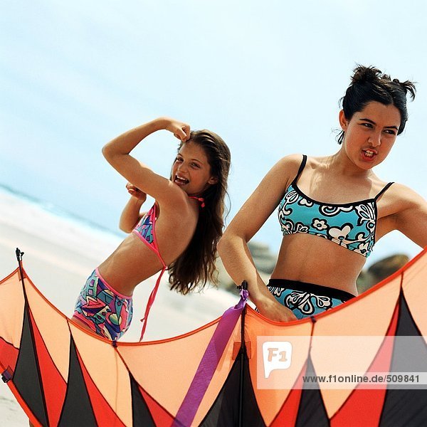 Mädchen im Badeanzug biegt Armmuskulatur  Teenager hält Drachen am Strand