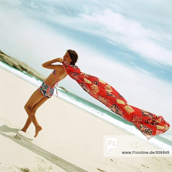 Mädchen im Badeanzug am Strand mit Sarong im Wind